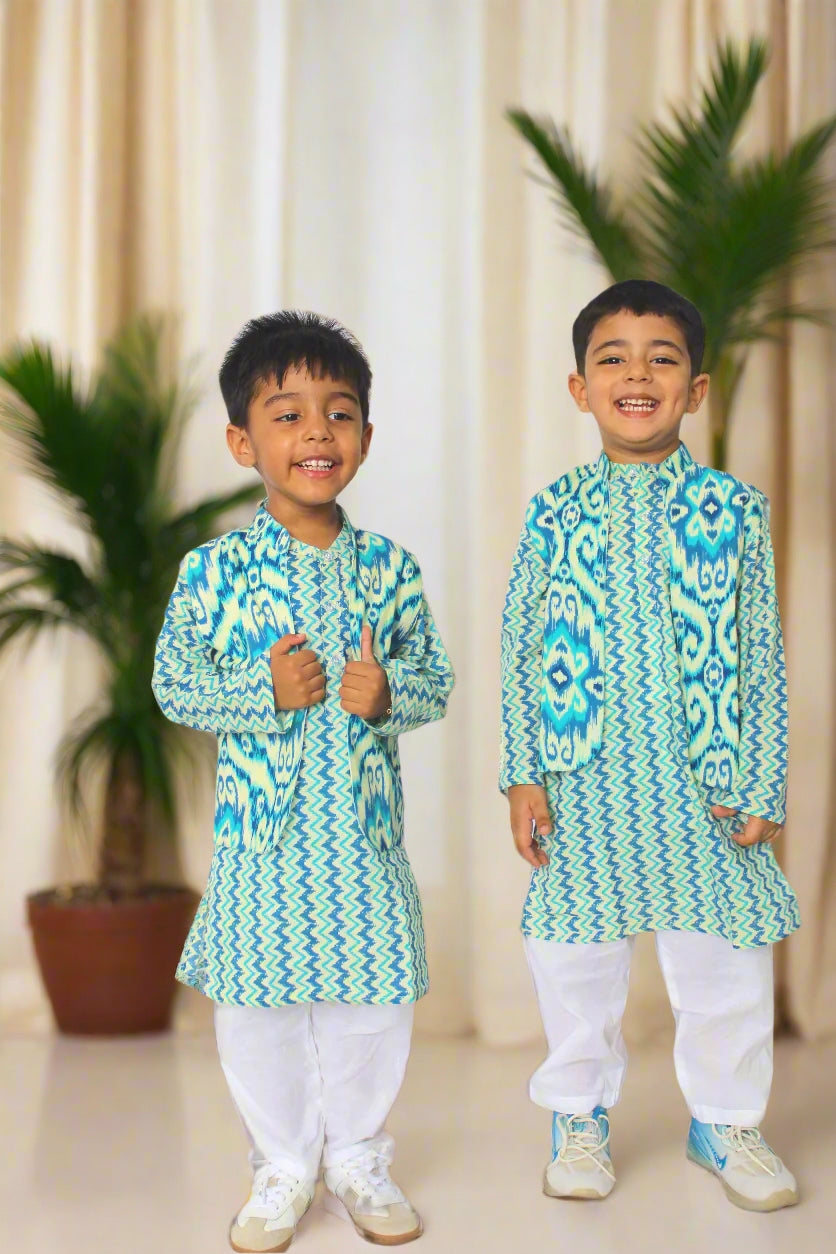 Two children wearing matching green and blue patterned outfits on a brown background