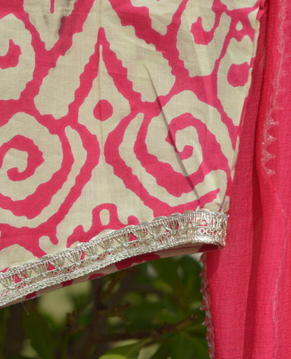 Pink fabric with a decorative pattern and border against a blurred green background