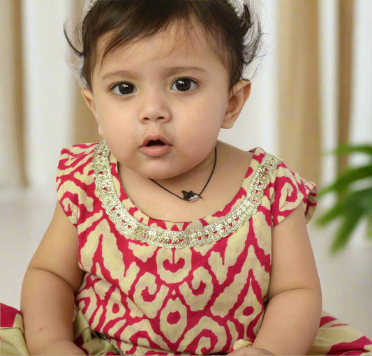 Baby wearing a pink and red patterned dress with a white background