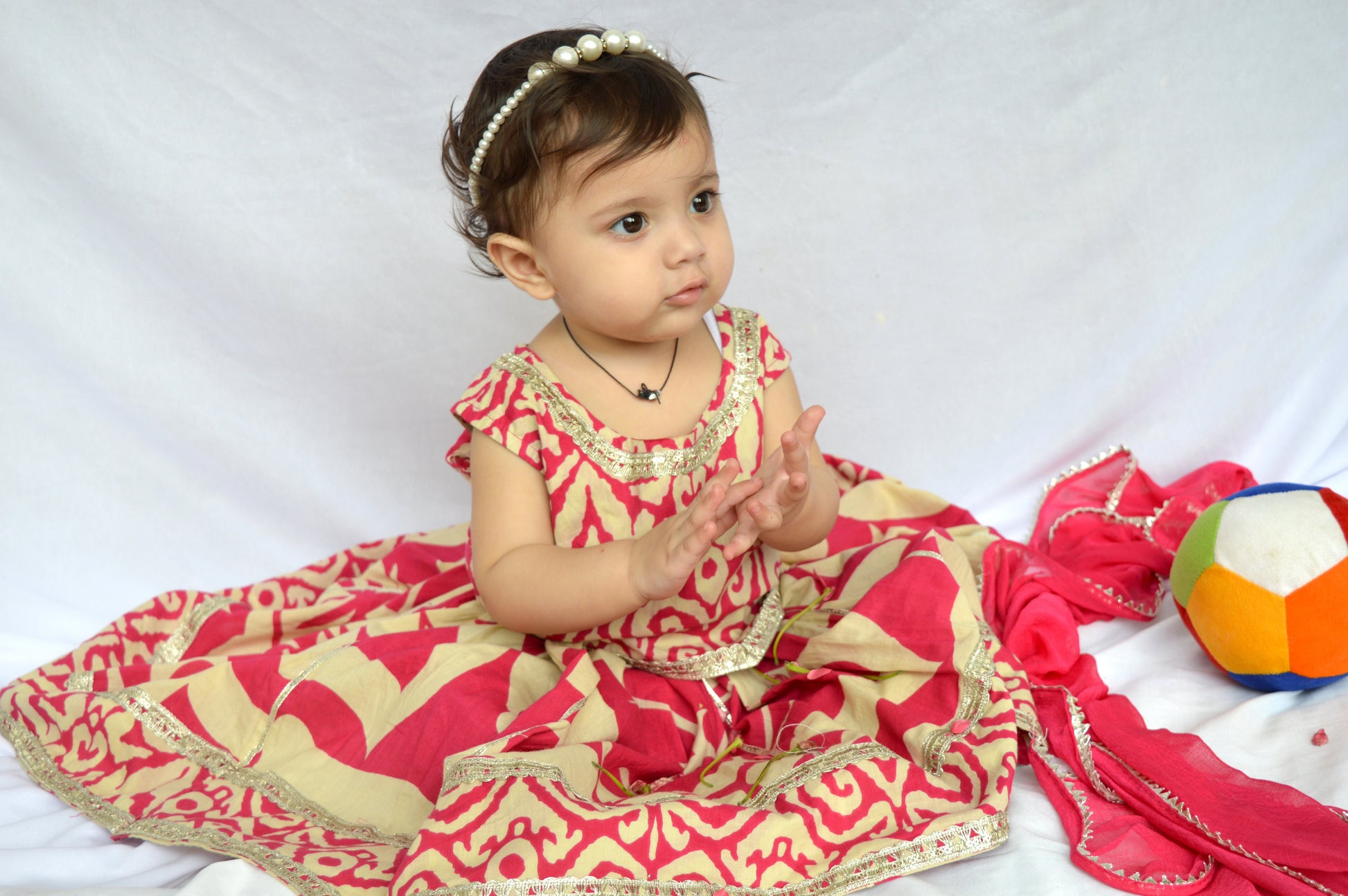 Baby in a red and beige traditional outfit with a colorful ball on a white background
