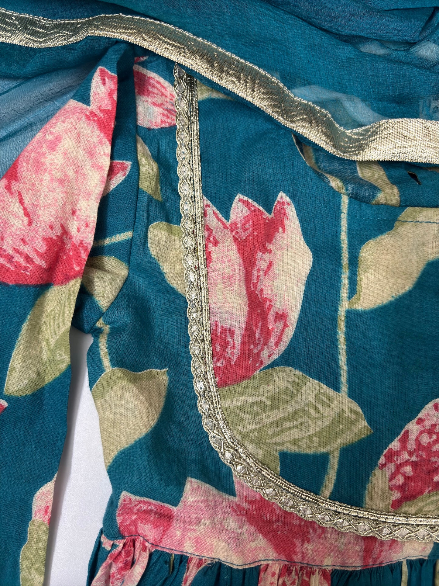 Close-up of a blue fabric with pink floral patterns and decorative trim.